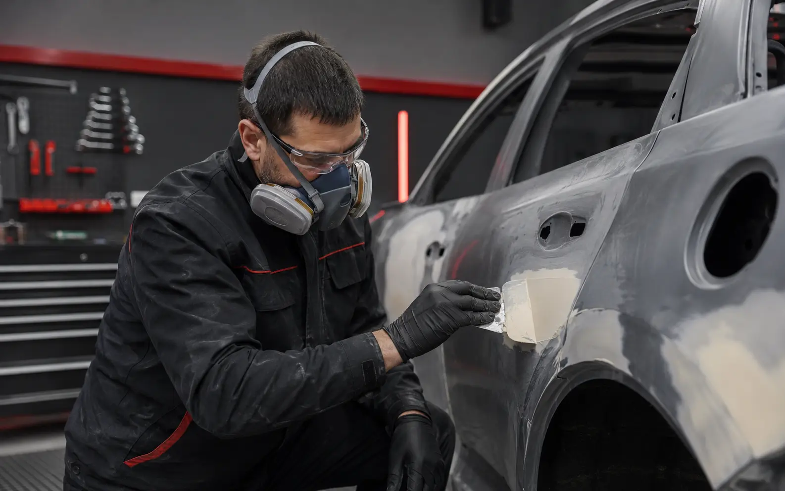Preparador automotriz aplicando masilla sobre la chapa de un vehículo